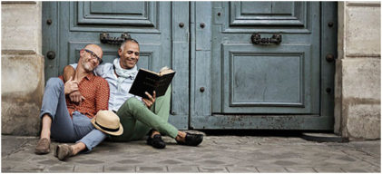 Mature Gay Couple Sitting Outside Reading A Book Together